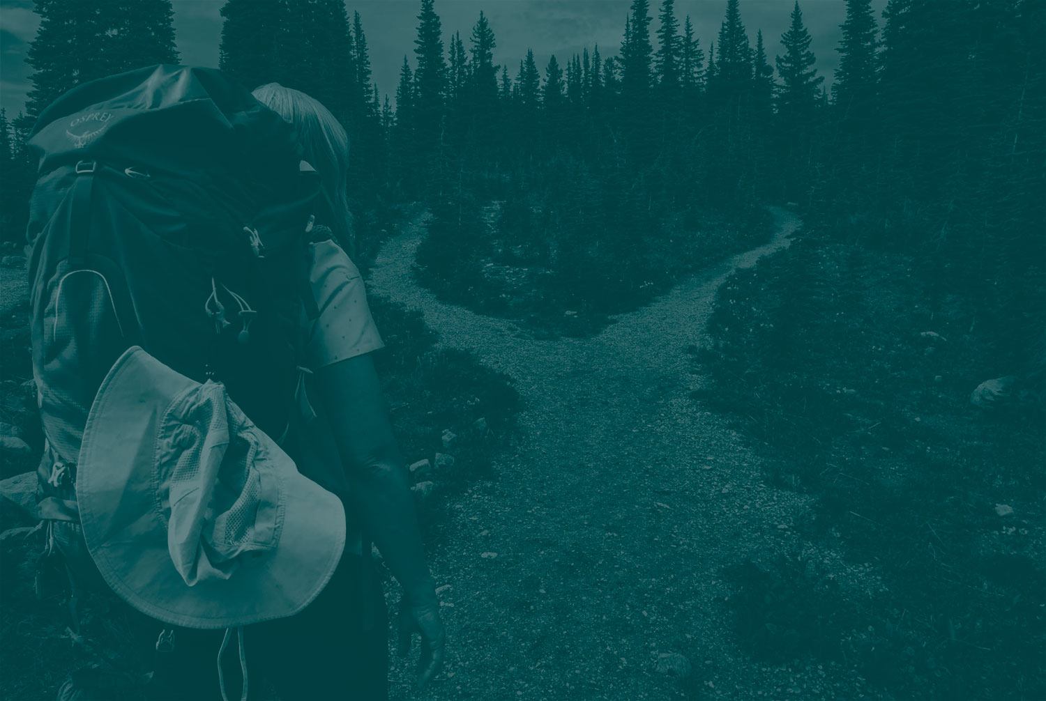 A woman carrying a camping backpack walking a pathway approaches a fork in the road