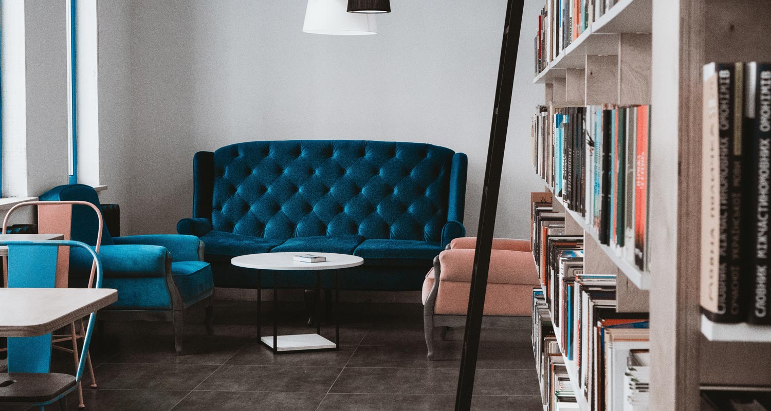 Small meeting space with a navy blue velvet sofa, a light blue armchair, and a rose-coloured armchair around a small white table